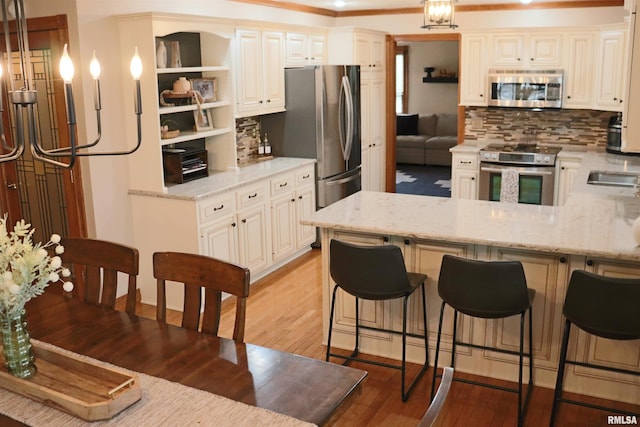 kitchen featuring light stone countertops, light wood finished floors, a peninsula, stainless steel appliances, and decorative backsplash