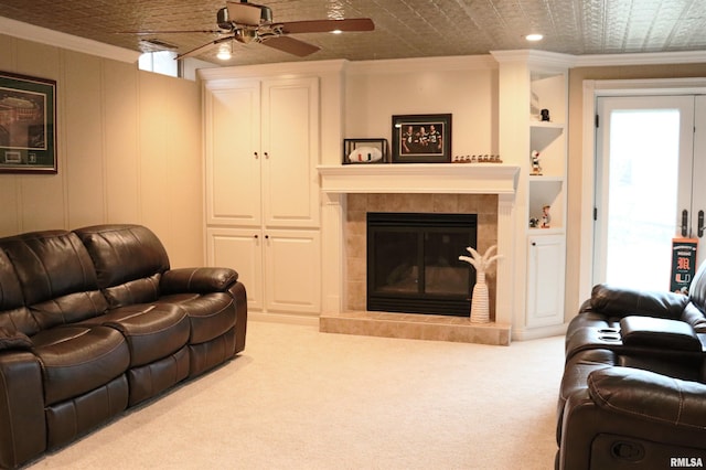 living area featuring a ceiling fan, a tiled fireplace, an ornate ceiling, carpet, and crown molding