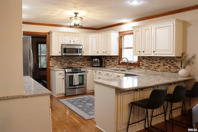 kitchen featuring light wood finished floors, a peninsula, a sink, appliances with stainless steel finishes, and crown molding