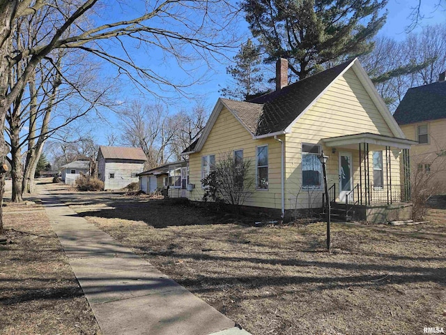 view of home's exterior with roof with shingles, a porch, and a chimney