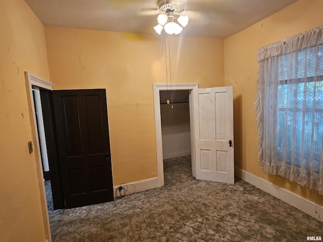 unfurnished bedroom with a spacious closet, baseboards, carpet, and a ceiling fan