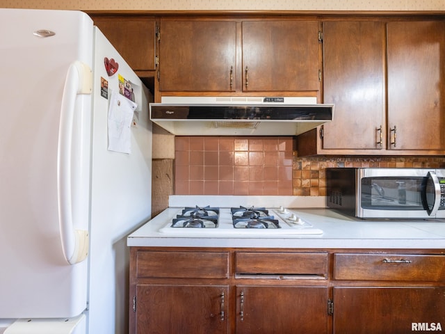 kitchen featuring under cabinet range hood, decorative backsplash, white appliances, and light countertops