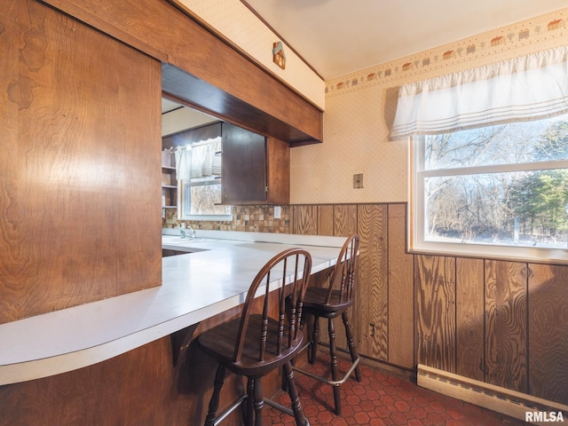 kitchen with wallpapered walls, a baseboard heating unit, a wainscoted wall, a breakfast bar, and a sink