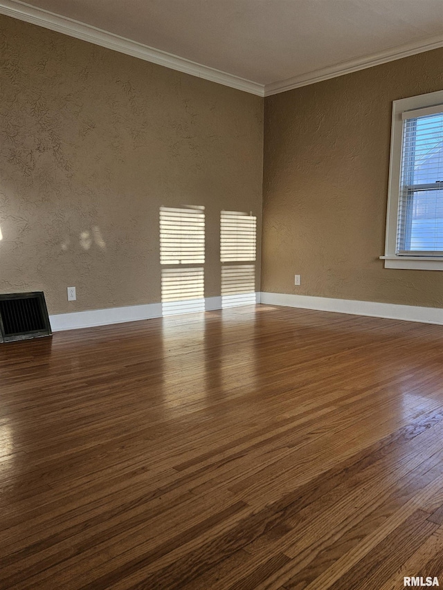 empty room with visible vents, ornamental molding, baseboards, dark wood-style flooring, and a textured wall