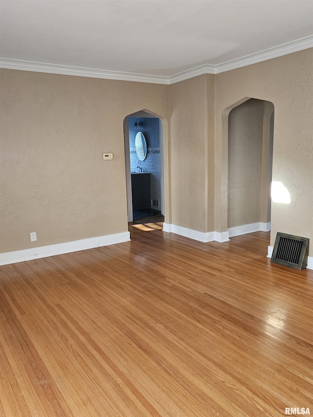 empty room featuring light wood-type flooring, visible vents, arched walkways, crown molding, and a textured wall