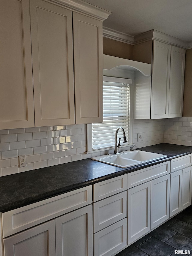 kitchen with a sink, decorative backsplash, dark countertops, and white cabinetry