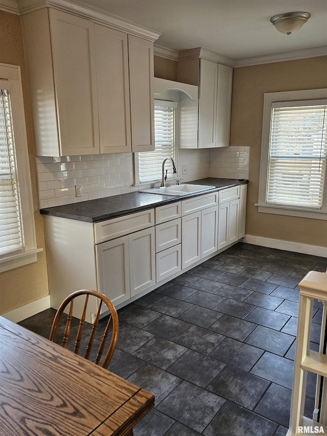 kitchen with dark countertops, ornamental molding, baseboards, and a sink