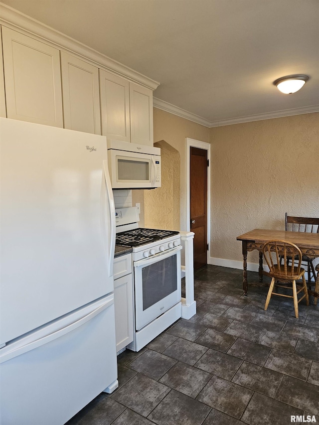 kitchen featuring baseboards, ornamental molding, a textured wall, white appliances, and white cabinetry