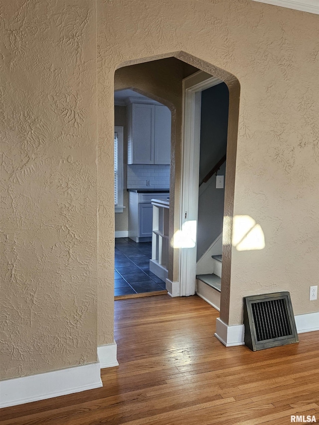 corridor with stairway, wood finished floors, visible vents, arched walkways, and a textured wall