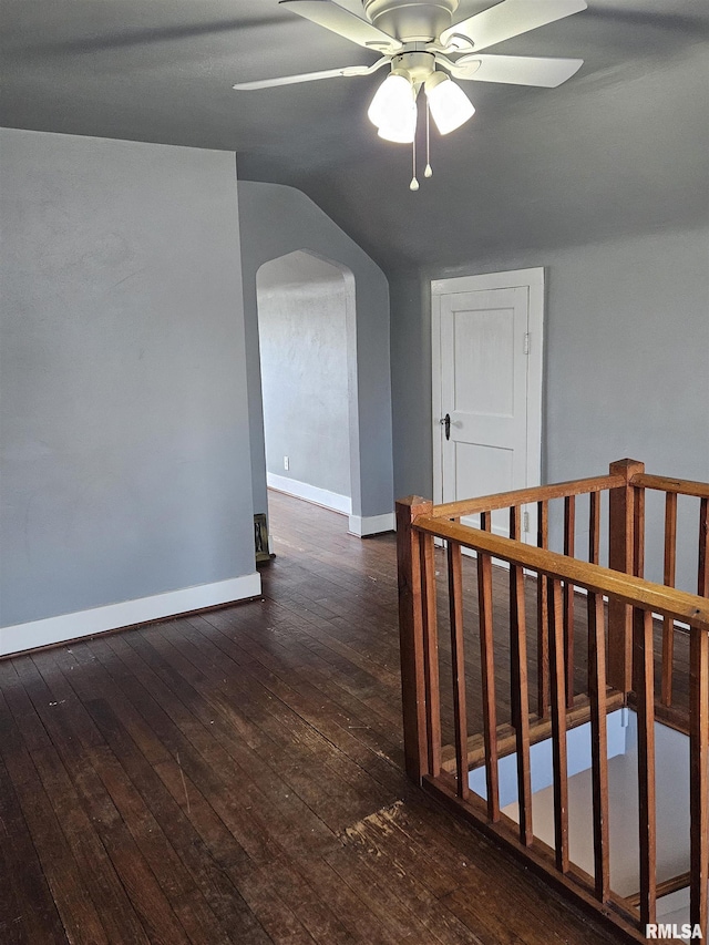 corridor with lofted ceiling, dark wood-style floors, arched walkways, and baseboards