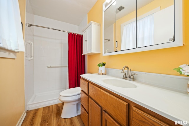 bathroom with visible vents, toilet, wood finished floors, a tile shower, and vanity