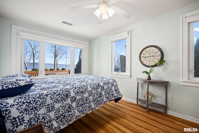 bedroom with wood finished floors, visible vents, a textured wall, and baseboards