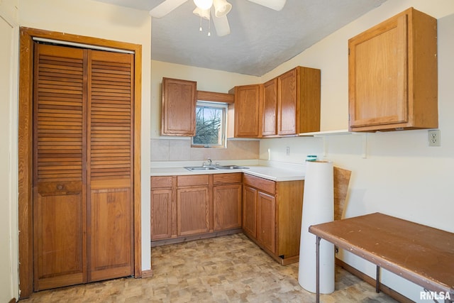 kitchen featuring a ceiling fan, light countertops, brown cabinetry, and a sink