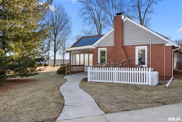 view of front of property with brick siding, roof mounted solar panels, a chimney, and fence