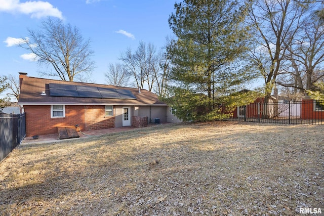 back of house featuring brick siding, roof mounted solar panels, a yard, a fenced backyard, and a patio area