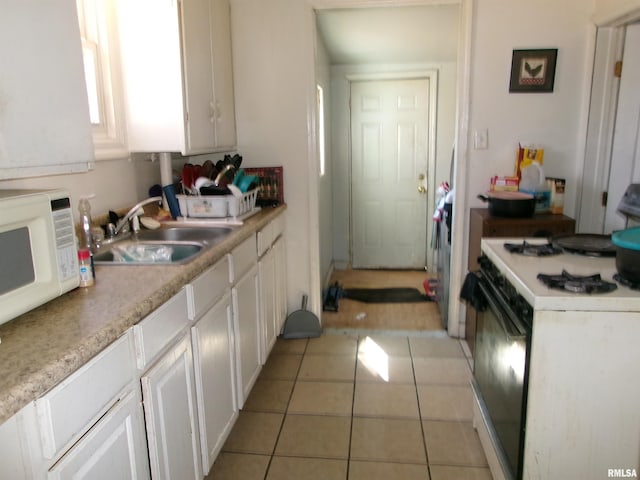 kitchen featuring white microwave, white cabinets, gas range oven, and a sink