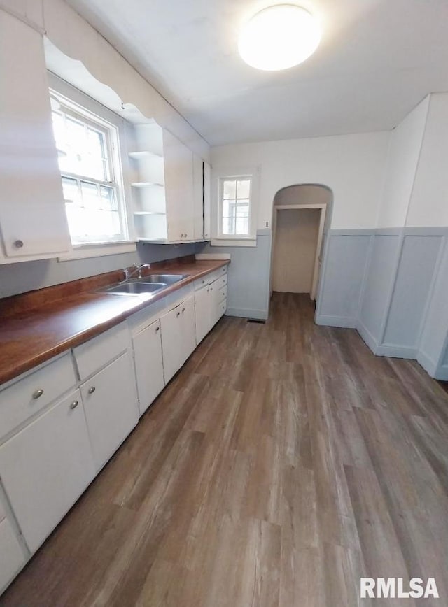 kitchen with light wood-type flooring, a sink, open shelves, arched walkways, and white cabinets