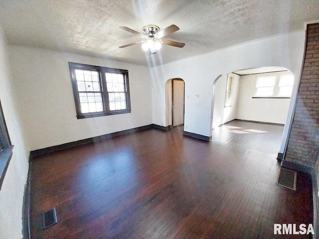 interior space featuring arched walkways, visible vents, a textured ceiling, and dark wood-style flooring