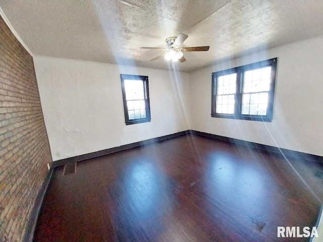 spare room featuring visible vents, a textured ceiling, dark wood-style floors, brick wall, and baseboards