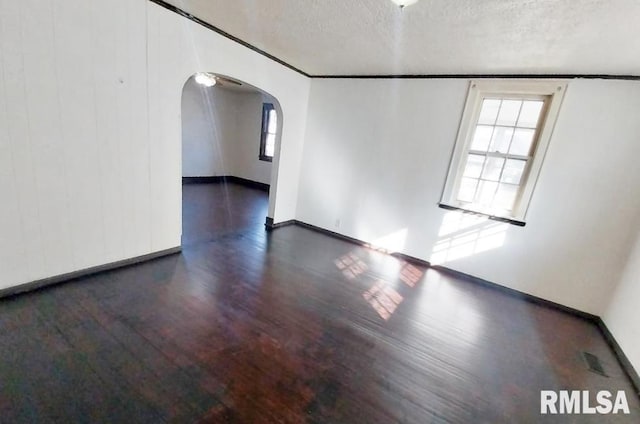 unfurnished room featuring arched walkways, plenty of natural light, and wood finished floors