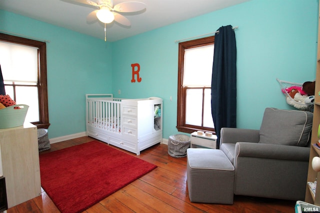 bedroom featuring multiple windows, a crib, baseboards, and hardwood / wood-style floors