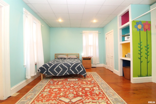 bedroom with a drop ceiling, baseboards, and wood finished floors