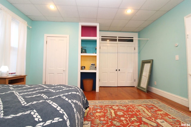 bedroom with a paneled ceiling, baseboards, and wood finished floors