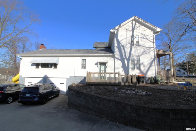 back of property with driveway, a chimney, a garage, and roof with shingles