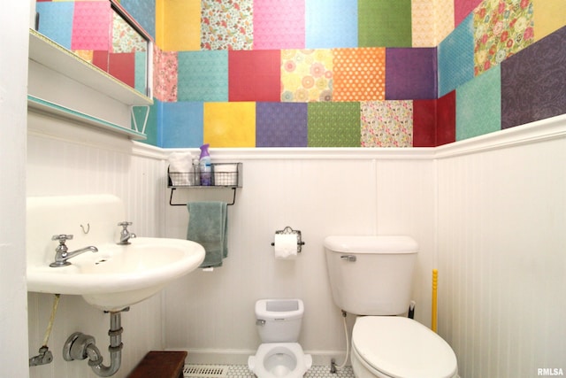 half bath with a wainscoted wall, toilet, and a decorative wall