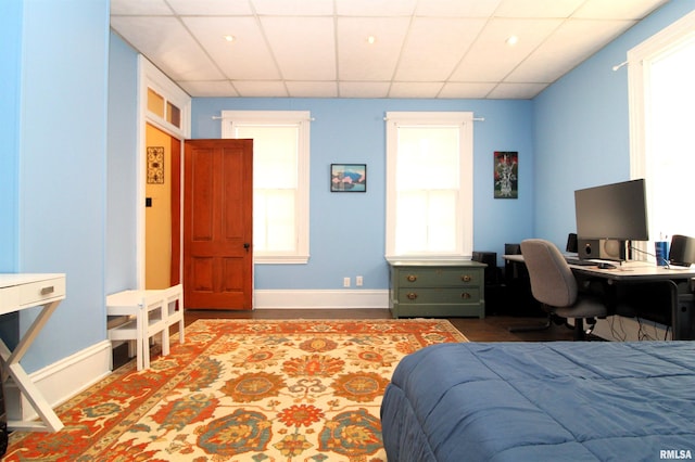 bedroom featuring wood finished floors, baseboards, and a drop ceiling