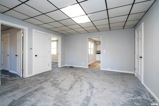 unfurnished bedroom featuring a drop ceiling, baseboards, multiple windows, and carpet flooring