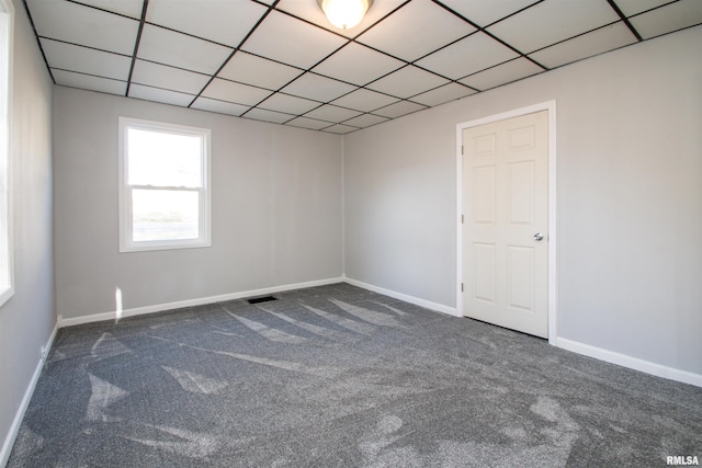 unfurnished room featuring dark colored carpet, visible vents, baseboards, and a drop ceiling