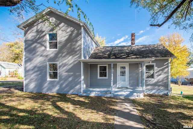 view of front facade with a front yard, a porch, and a chimney