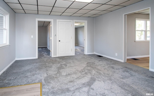 carpeted empty room featuring baseboards, visible vents, and a drop ceiling