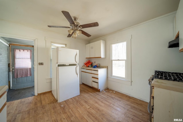 kitchen with gas range, light countertops, freestanding refrigerator, light wood-style floors, and white cabinets