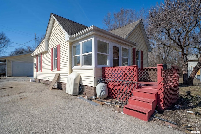 view of side of home with a detached garage, an outbuilding, roof with shingles, and a sunroom