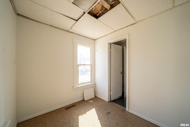 carpeted spare room with baseboards, visible vents, and a drop ceiling