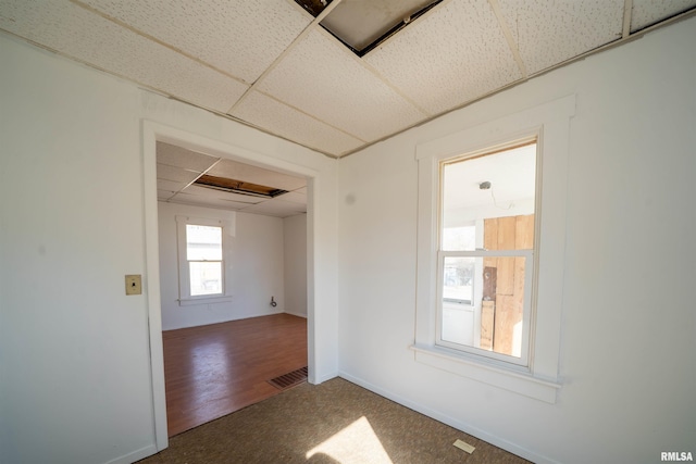 carpeted spare room with a drop ceiling, visible vents, and baseboards