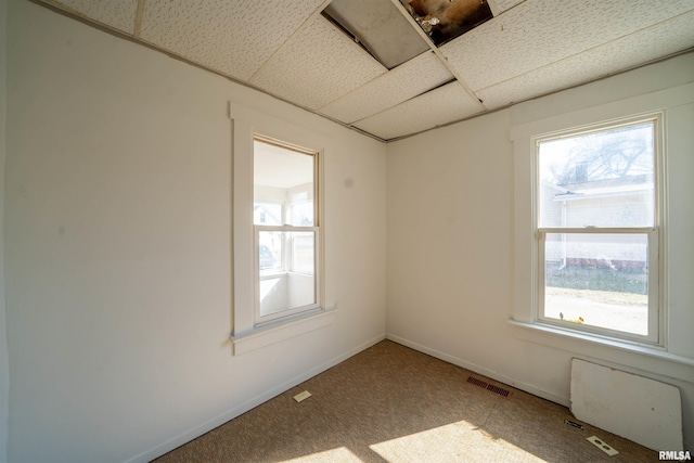 carpeted empty room with a wealth of natural light, visible vents, and a paneled ceiling