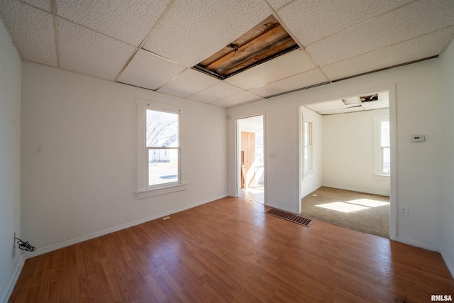 unfurnished room with a drop ceiling, baseboards, visible vents, and wood finished floors