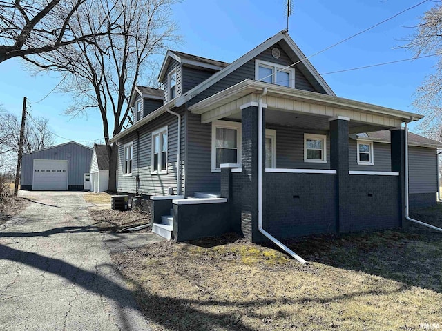 view of front facade featuring an outbuilding, aphalt driveway, a detached garage, brick siding, and central AC unit