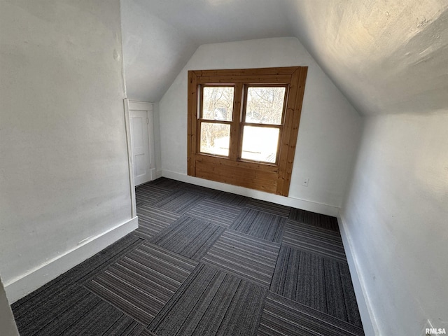 additional living space featuring lofted ceiling, baseboards, and dark carpet