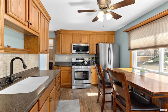 kitchen with dark wood-style flooring, a sink, decorative backsplash, appliances with stainless steel finishes, and dark countertops