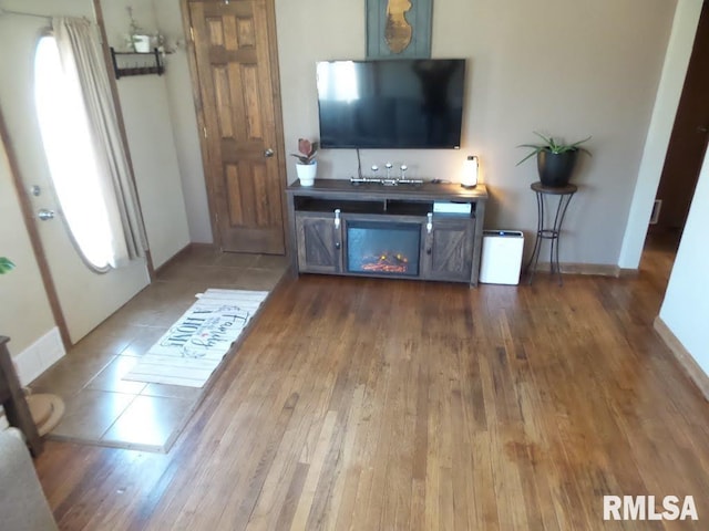 living room with a warm lit fireplace, baseboards, and wood finished floors