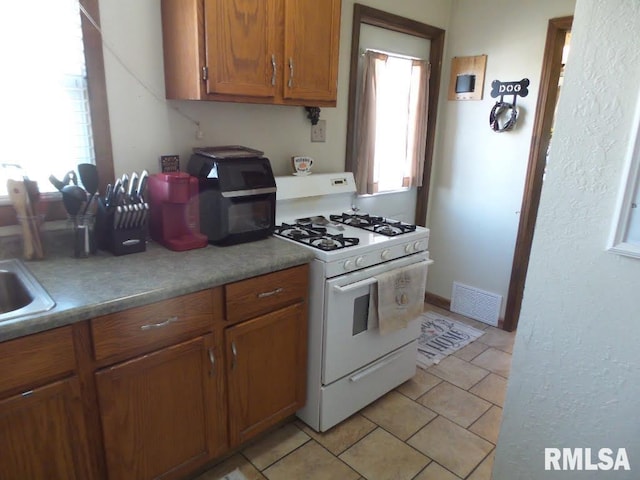 kitchen with visible vents, light tile patterned flooring, light countertops, white gas range oven, and brown cabinets