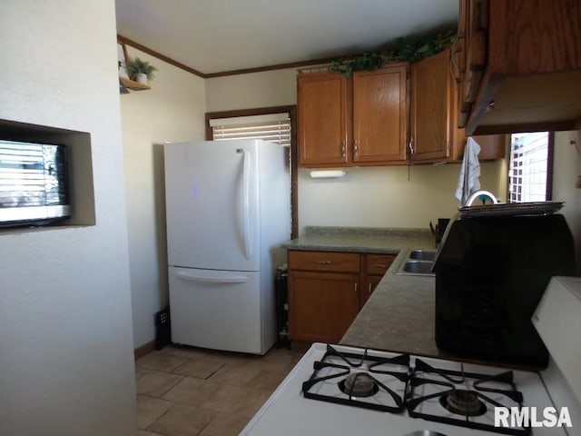 kitchen with brown cabinets, crown molding, freestanding refrigerator, and a sink