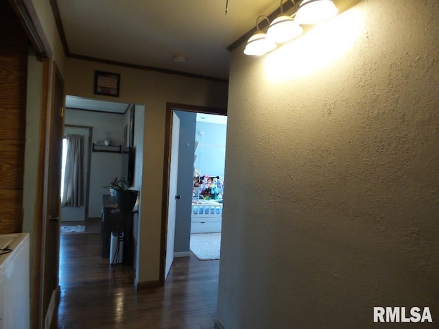 hallway featuring a chandelier, dark wood-style flooring, a textured wall, and ornamental molding