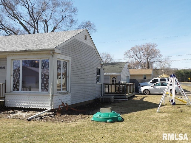 view of side of property with a lawn, a wooden deck, a playground, and roof with shingles