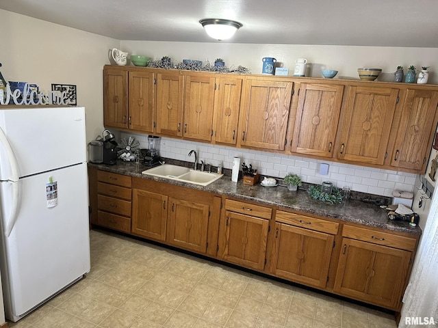 kitchen with a sink, dark countertops, brown cabinetry, and freestanding refrigerator