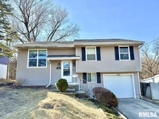 split foyer home featuring a garage, a shingled roof, concrete driveway, and fence